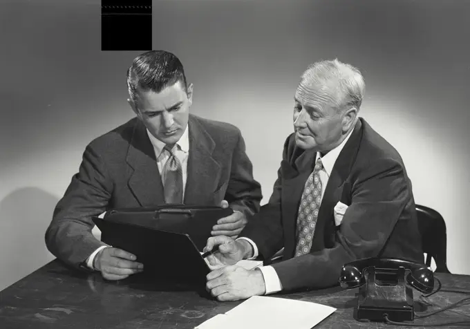 Vintage photograph. young man and older man sitting together at desk discussing papers