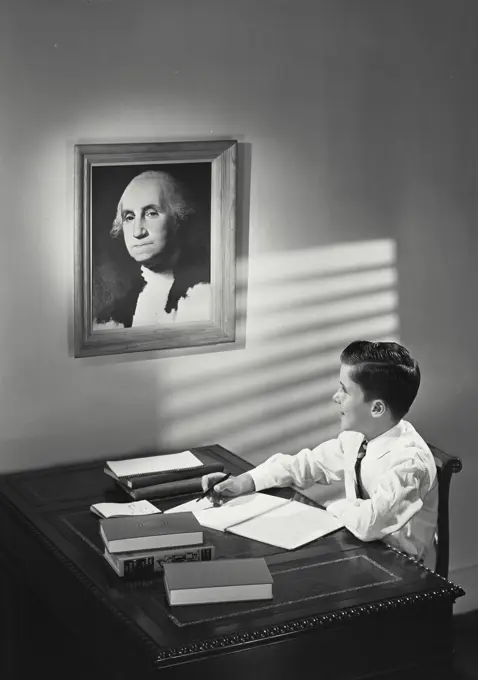 Vintage photograph. young boy sitting at desk looking at painting of George Washington.