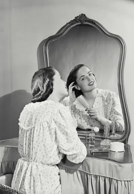 Vintage photograph. Woman in night gown adjusting hair in mirror.