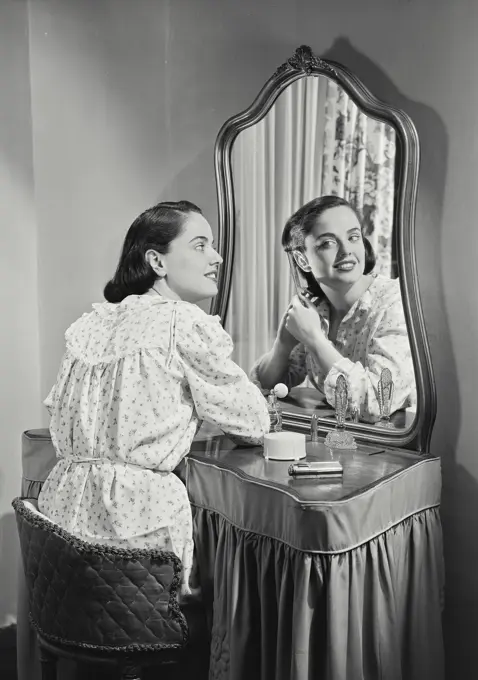 Vintage photograph. Woman in night gown adjusting hair in mirror.