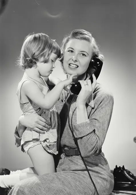 Vintage photograph. Daughter plays with mouthpiece while mother talks on phone