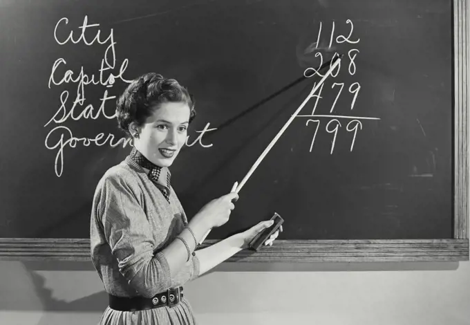 Vintage photograph. Teacher standing at chalkboard pointing to numbers