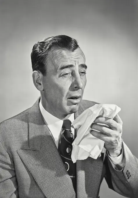 Vintage photograph. Man in suit and tie sneezing into handkerchief