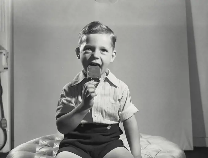 Vintage photograph. Little boy taking bite out of ice cream pop.