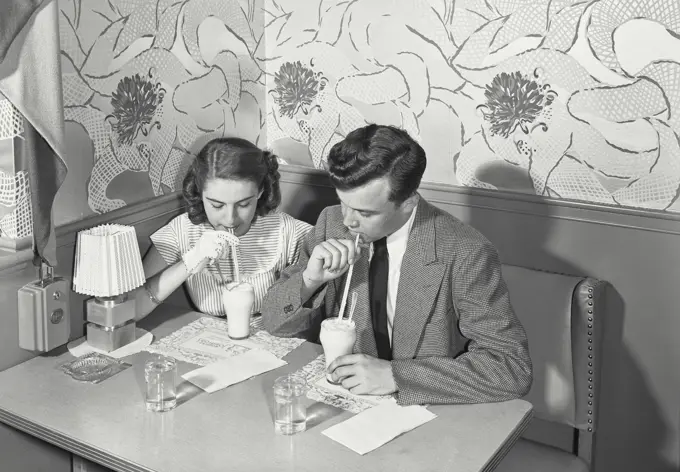 Vintage photograph. Young couple sipping milkshakes at restaurant booth