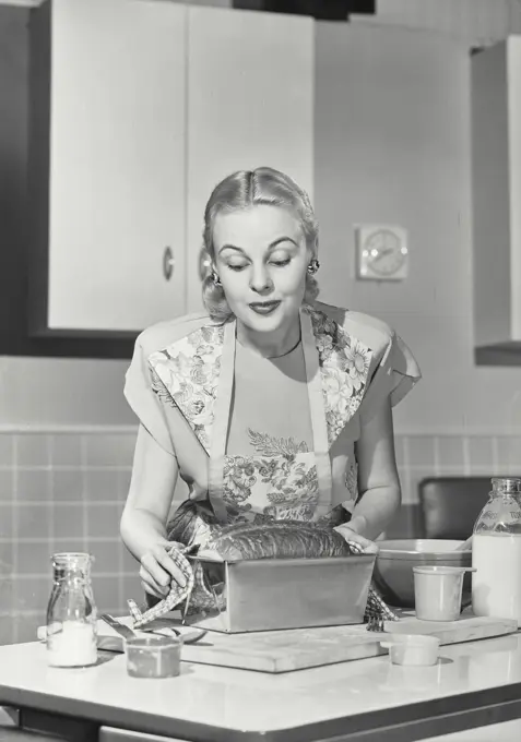 Vintage photograph. Woman in kitchen holding loaf of bread.