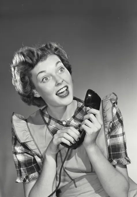 Vintage photograph. Woman in apron holding phone call with excited expression.