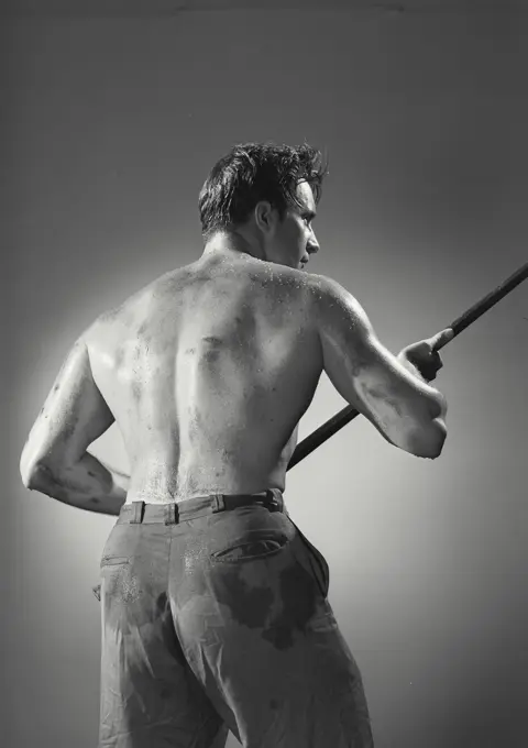 Vintage photograph. Back view of shirtless man holding pipe