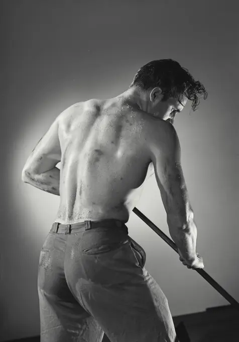 Vintage photograph. Back view of shirtless man holding tool