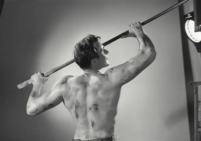 Vintage photograph. Back view of shirtless man holding tool