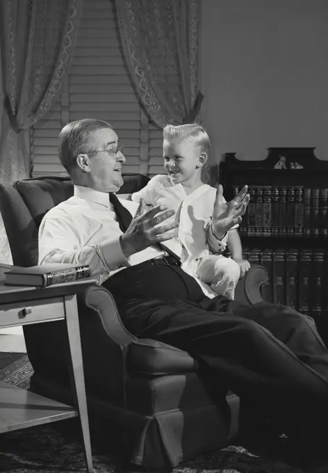 Vintage photograph. Man telling story to young boy on his lap