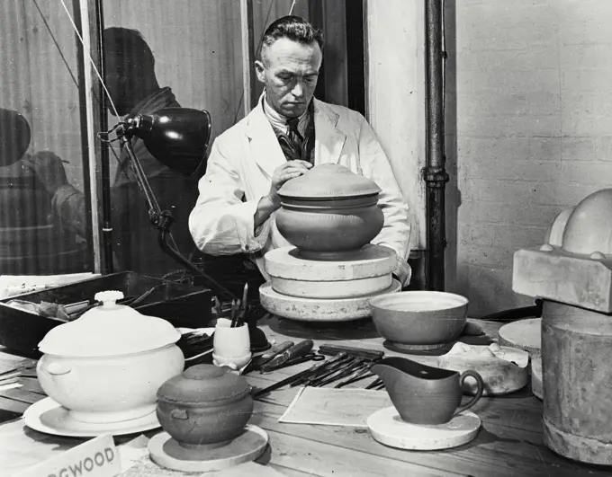 Vintage photograph. British Pottery Industry worker putting finishing touches to a cast for a soup toureen. On the left can be seen the original as it left the designer's hands