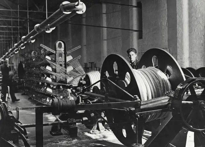 Vintage photograph. Rope strand being formed on a large House Machine. Note the size of the bobbin taking the strand. This bobbin weighs approximately one ton before being filled.