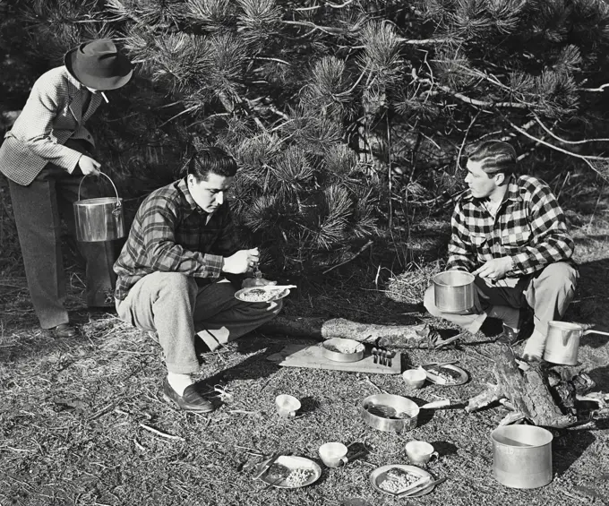 Vintage photograph. Two men and a women having a camp picnic in the woods