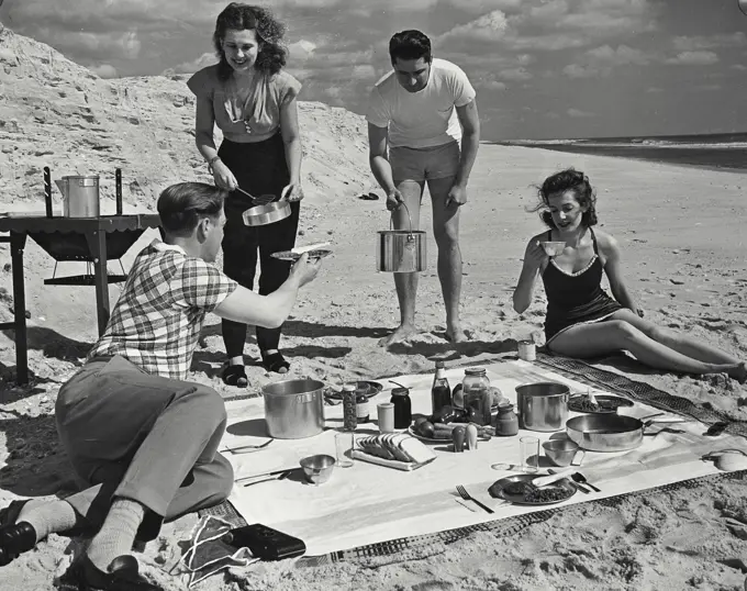 Vintage photograph. Two men and two women cooking on grill for picnic at the beach