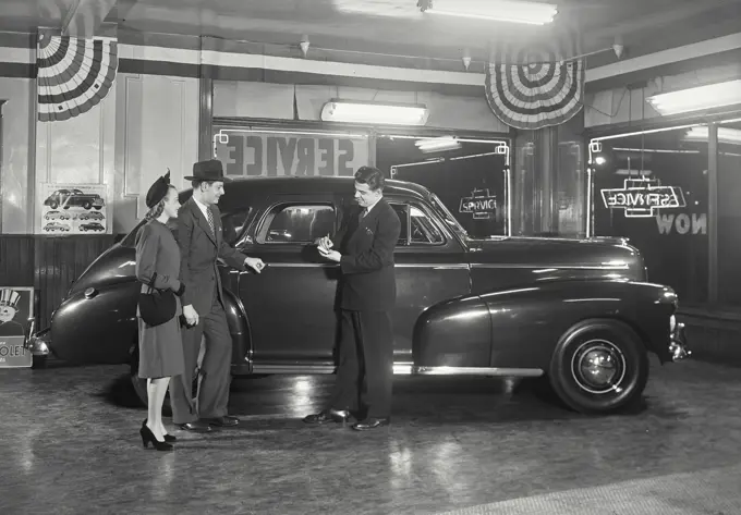 Vintage photograph. Couple in car dealership standing next to Chevrolet Stylemaster talking to salesman