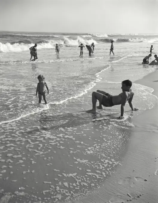 Vintage photograph. Boy crab-walking at beach with younger boy watching