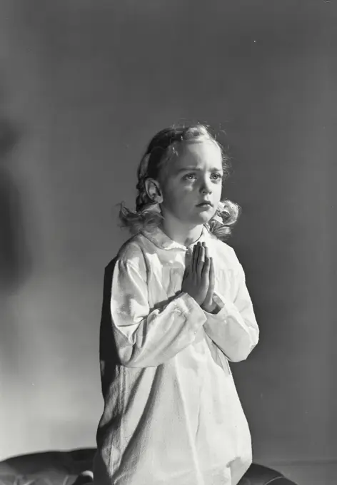 Vintage photograph. Young girl with blonde hair kneeling and praying