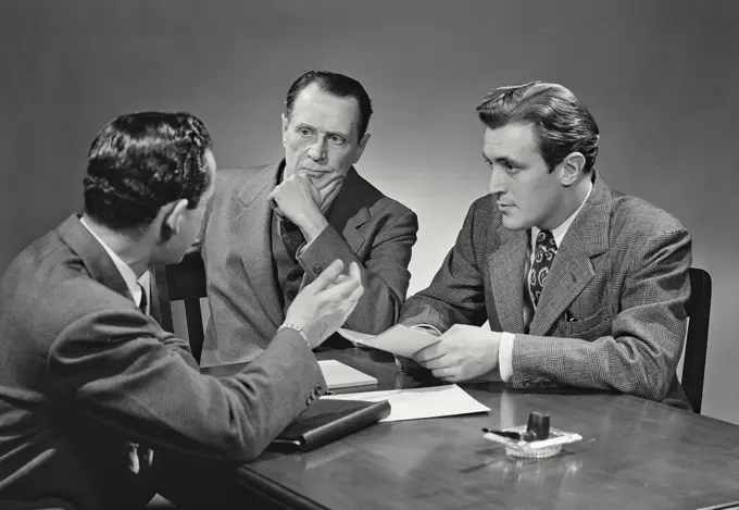 Vintage photograph. Group of men in suits sitting at desk having business discussion