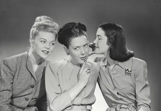 Vintage photograph. Three women wearing office attire telling secrets