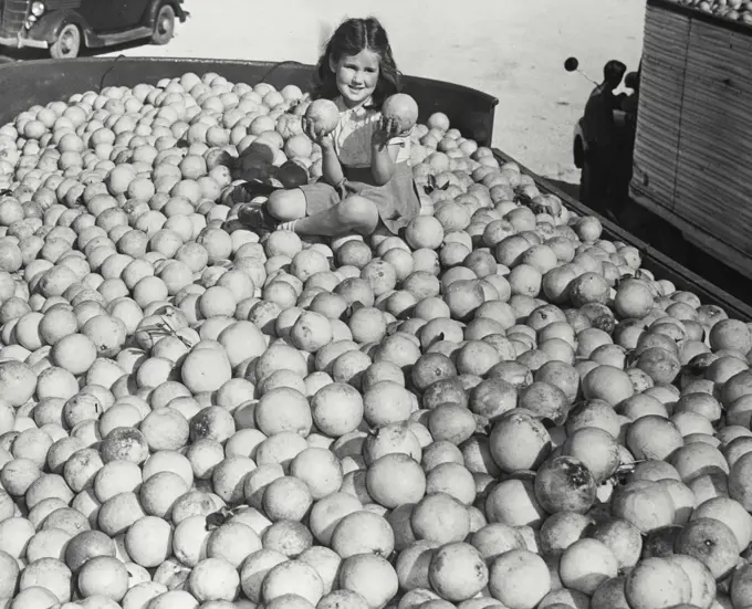 Young girl sitting in the middle of 24,000 pounds of grapefruits, ready to be canned and shipped all over the world