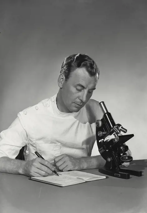 Scientist using notebook while at microscope