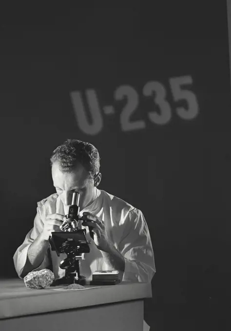 Scientist looking through microscope with U-235 (Uranium Isotope) being projected on the wall