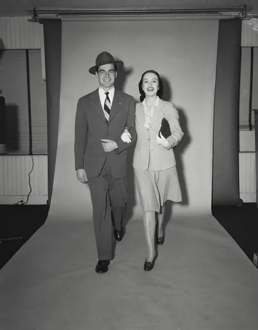 Man in a suit walking with woman in dress holding arm