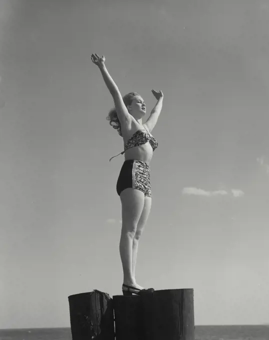 Woman in swimsuit standing on post with hands in air
