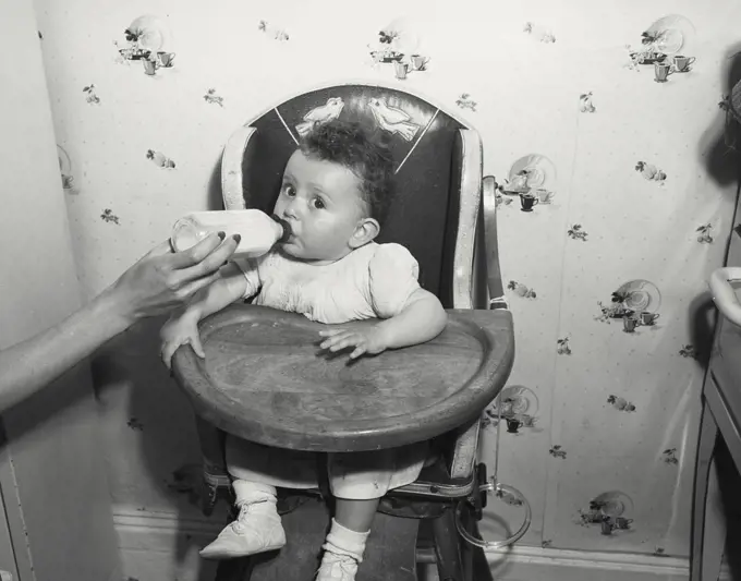 Baby in high chair drinking from bottle