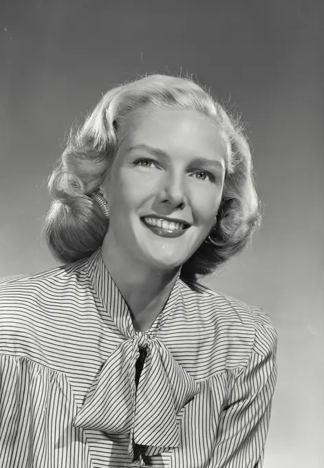 Woman in striped blouse with bow smiling at camera.