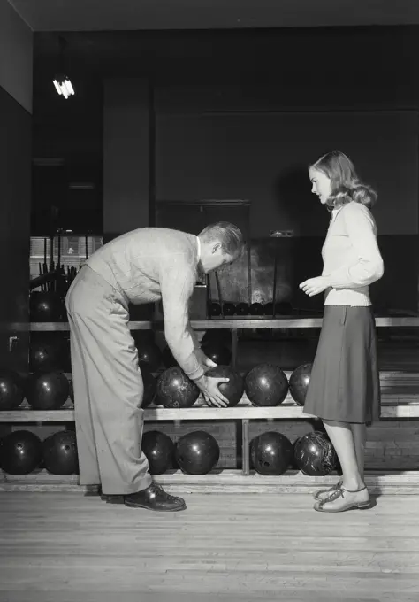 Man grabbing bowling ball from shelf for woman