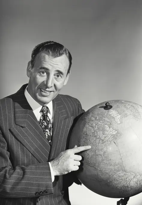 Dark haired caucasian man wearing pin striped suit pointing with index finger at United States of America on globe