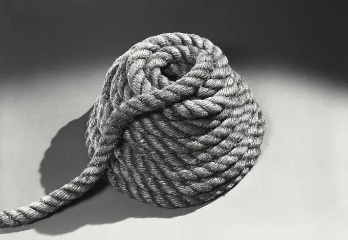 Vintage photograph. Rope coiled in pile on solid surface with dark shadow at top