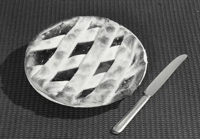 Vintage photograph. Pie with woven crust sitting on table with knife