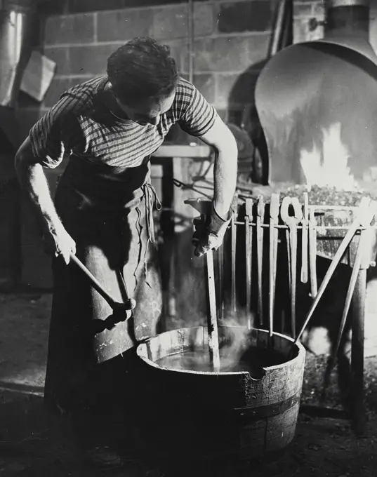 Vintage photograph. Blacksmith seen dunking red hot steel in water bath