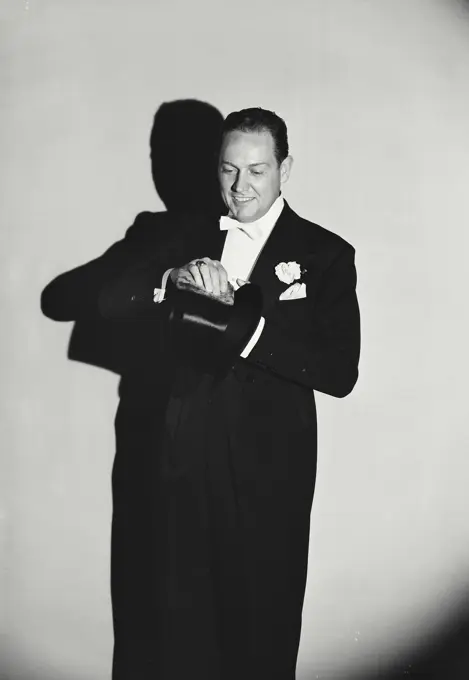 Vintage Photograph. Smiling man wearing tuxedo cleaning top hat with rag