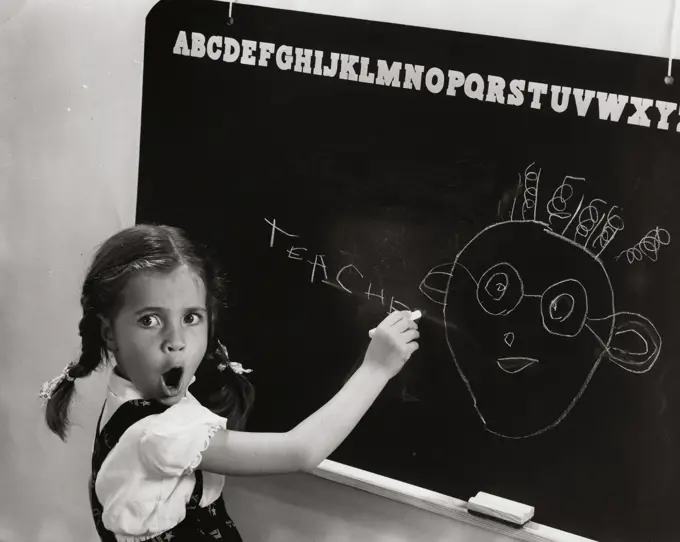 Side profile of a girl drawing a cartoon of her teacher on the blackboard