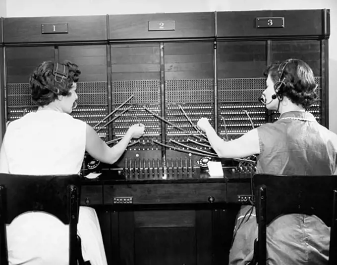 Rear view of two female telephone operators operating a telephone switchboard