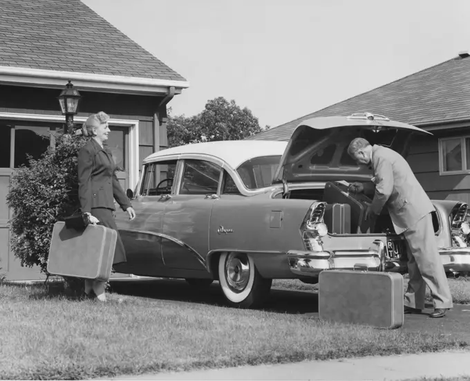 Senior couple loading luggage into car trunk