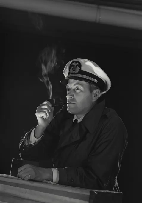 Vintage Photograph. Man in captains uniform smoking pipe and looking off camera