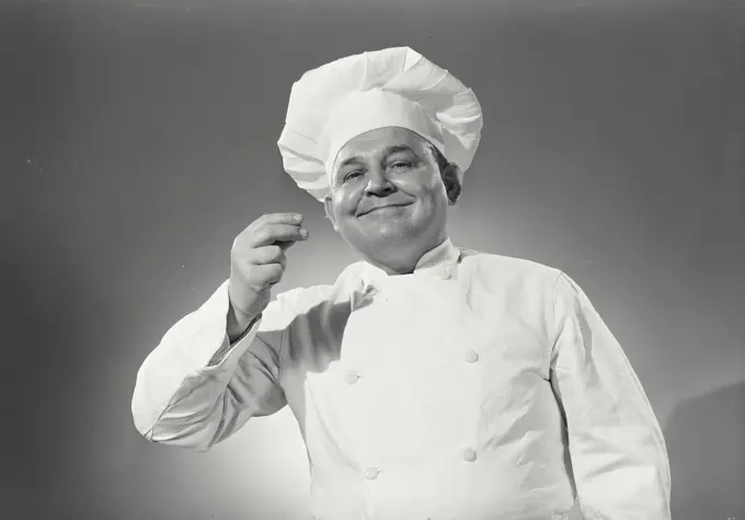 Vintage Photograph. Man in chefs uniform tasting an imaginary spoon