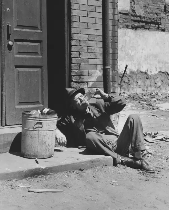 High angle view of a homeless senior man drinking alcohol sitting near a garbage can