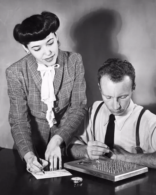 Vintage Photograph. Woman recording data from aptitude test being performed by man sitting next to her. This test measures to a fine degree Finger Dexterity, Tweezer Dexterity, and Eye and Hand Coordination