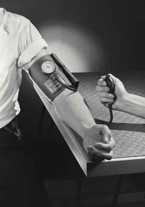 Vintage Photograph. Male hand with shirt rolled up demonstrating a Tycos Blood Pressure cuff with other hand pumping, Frame 1