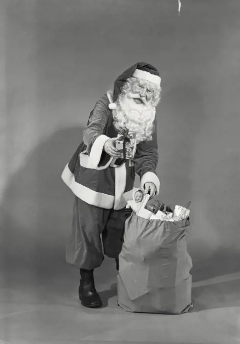 Vintage photograph. Man in Santa Claus costume grabbing Christmas toys from sack