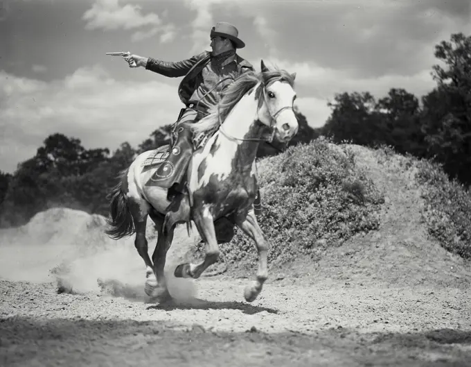 Vintage Photograph. Man in chaps riding on horses back shooting gun. Frame 1