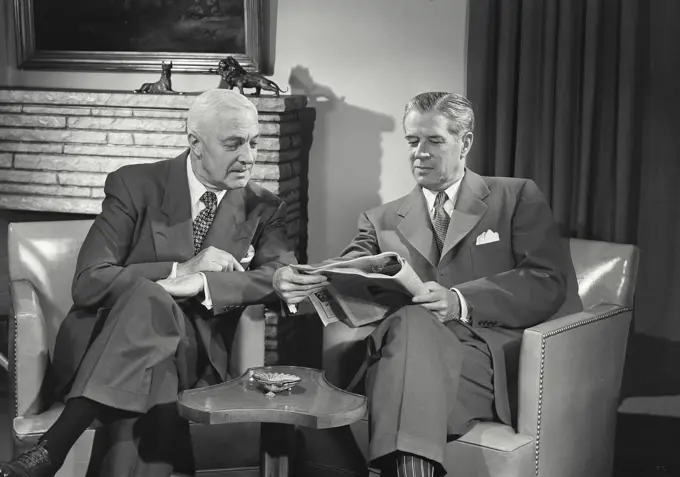 Vintage Photograph. Men in suits sitting in chairs talking with each other and reading newspaper