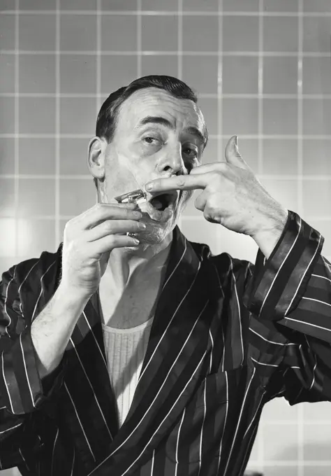 Vintage photograph. Man in robe shaving in bathroom