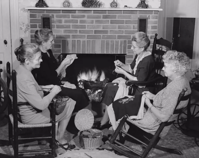 Senior women sitting in chairs near a fireplace and knitting